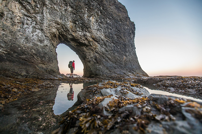 low angle of backpacker standing in Hole-in-the-Wall, Rialto Beach, by Cavan Images / Christopher Kimmel / Alpine Edge Photography