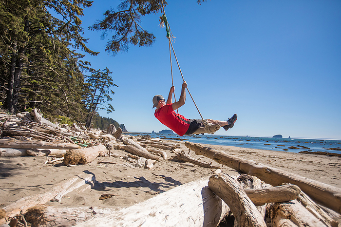 man swinging on driftwood swing in Olympic National Park, by Cavan Images / Christopher Kimmel / Alpine Edge Photography