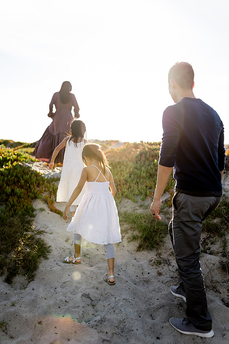 Family of Four Walking Through Dunes on Beach at Sunset, by Cavan Images / Jill Denny Soto