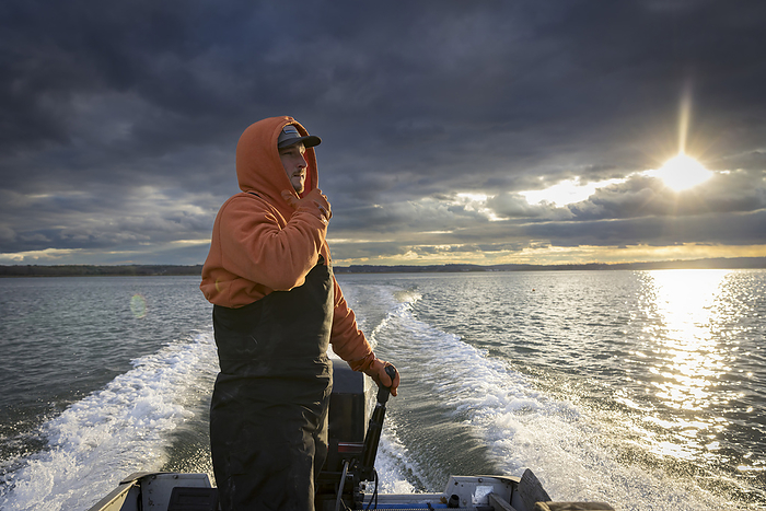 Commercial fisherman wearing waders in fishing boat with stormy skies, by Cavan Images / Julia Cumes