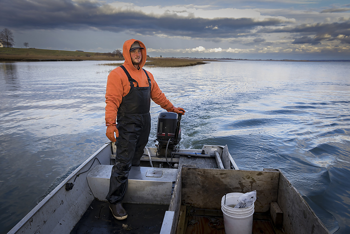 Commercial fisherman wearing waders in fishing boat with stormy skies, by Cavan Images / Julia Cumes