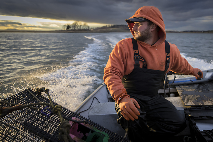 Commercial fisherman driving fishing boat with stormy skies, by Cavan Images / Julia Cumes