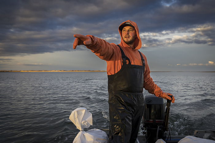 Commercial fisherman in boat pointing to something in the distance, by Cavan Images / Julia Cumes