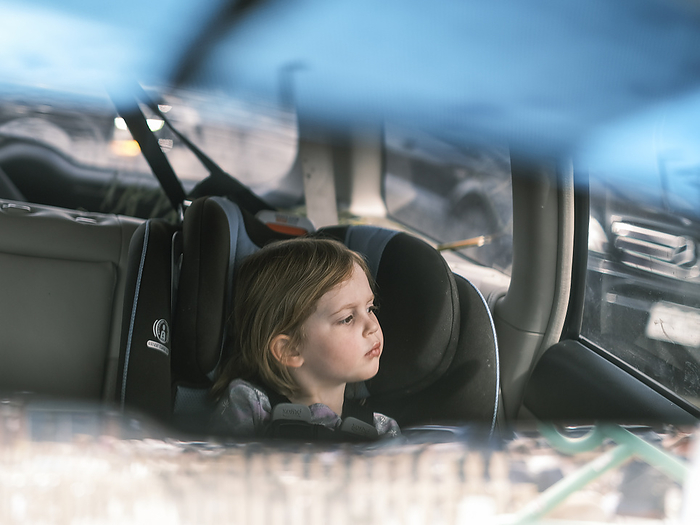Young girl driving car in the backseat, by Cavan Images / Patrick Lienin