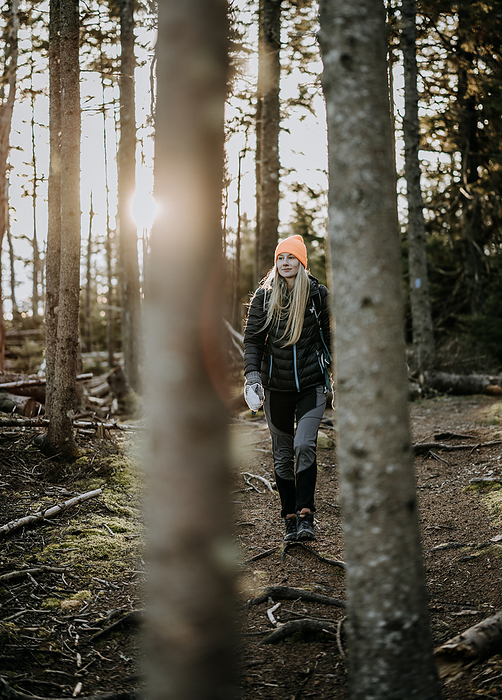 blonde female hikes along woods trail as sun sets, Maine, by Cavan Images / Chris Bennett