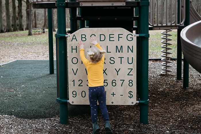 Young child playing with alphabet structure on park playground, by Cavan Images / Krista Taylor