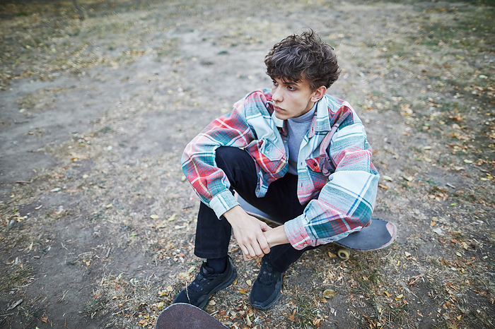 contemplative young man sitting on a skateboard, by Cavan Images / Elena Perevalova