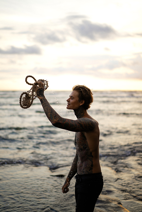 Young handsome tattooed man on the beach, Bali., by Cavan Images / Yuliya Kirayonak