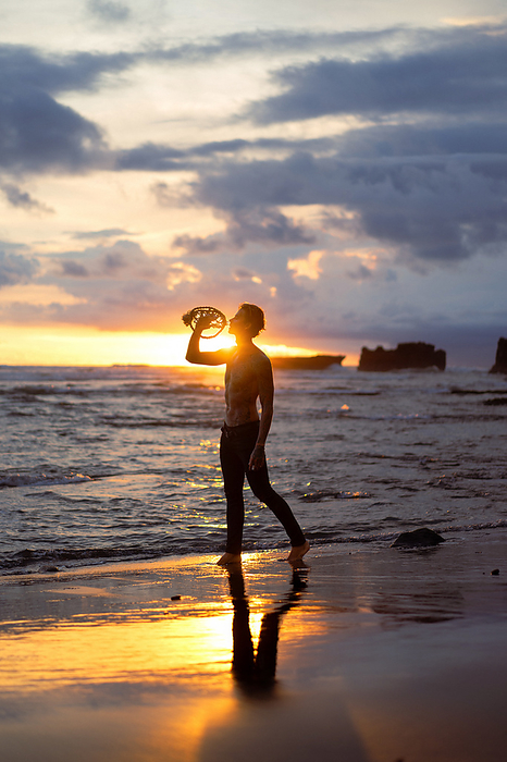 Young handsome tattooed man on the beach drinking water, Bali., by Cavan Images / Yuliya Kirayonak