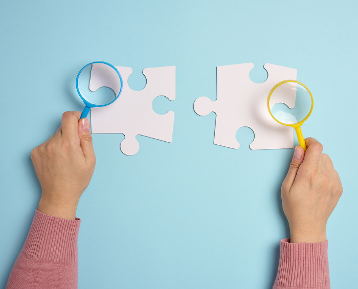 White empty puzzles and a magnifying glass in hand on a blue background, top view White empty puzzles and a magnifying glass in hand on a blue background, top view