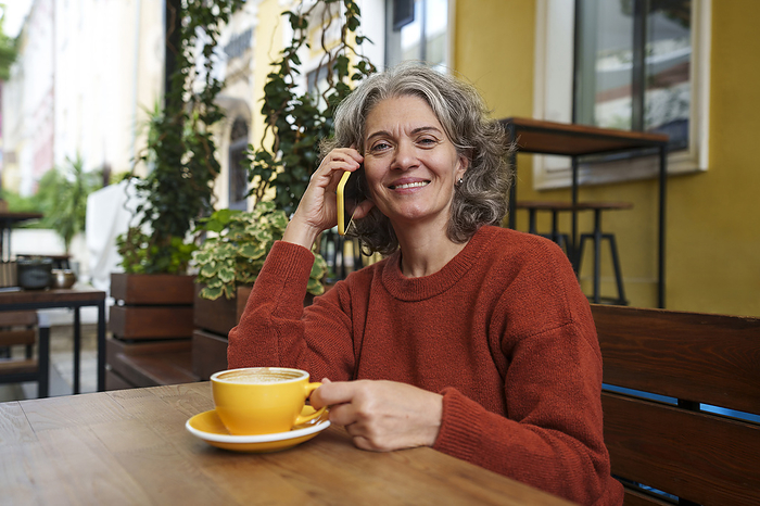 Smiling woman talking on smart phone at sidewalk cafe