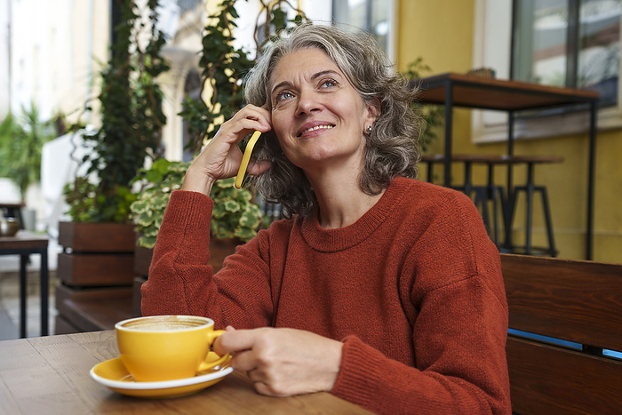Smiling mature woman talking on smart phone at sidewalk cafe