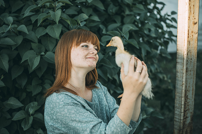 Smiling young redhead woman with freckles looking at duckling