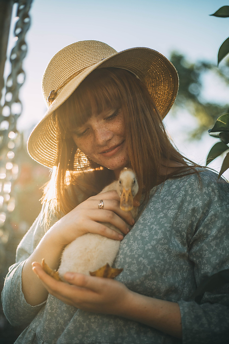 Young woman wearing hat holding duckling