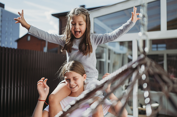 Smiling girl carrying sister on shoulders in front of house