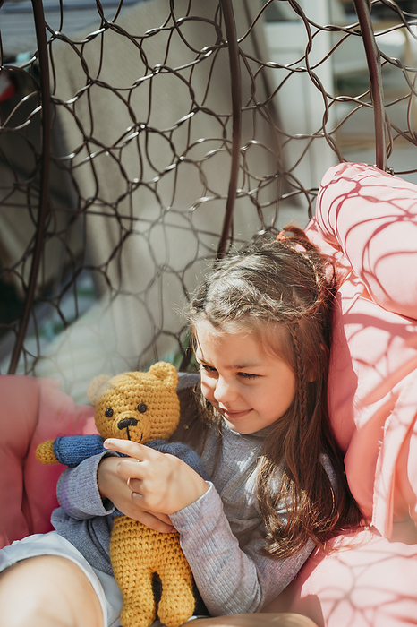 Smiling girl playing with stuffed toy in porch swing