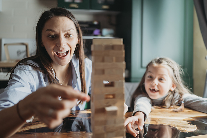 Smiling mother and daughter playing block removal game at home