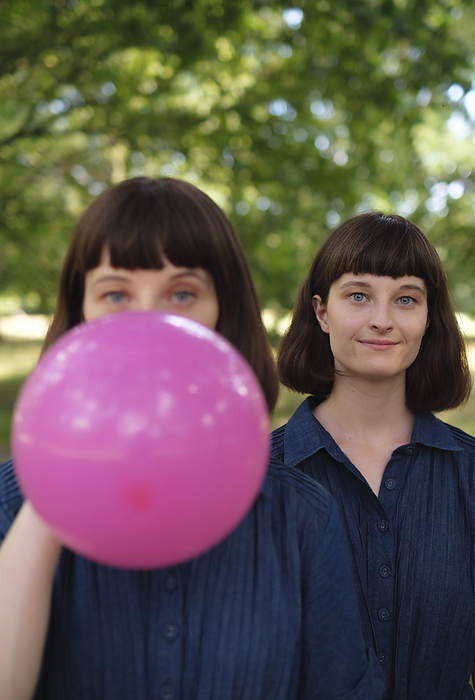 Smiling young woman with sister blowing pink balloon in park