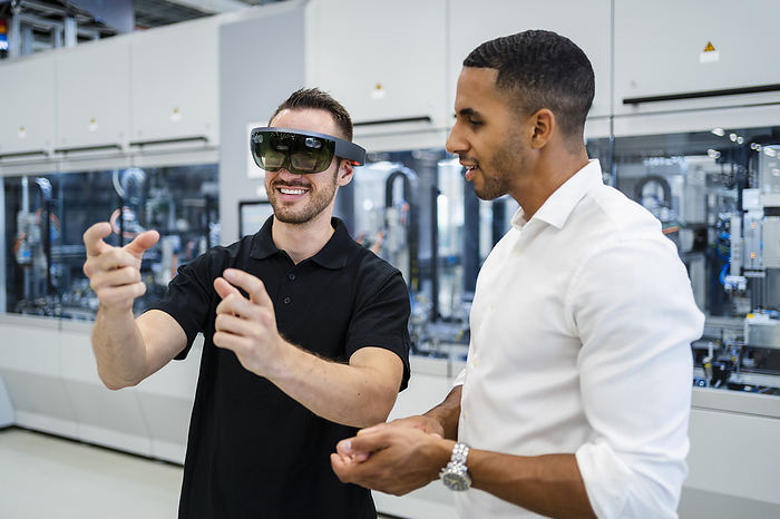 Technician wearing augmented reality glasses in a factory interacting with colleague