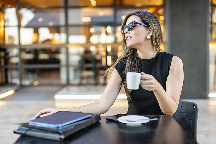 Businesswoman wearing sunglasses and holding coffee cup at sidewalk cafe