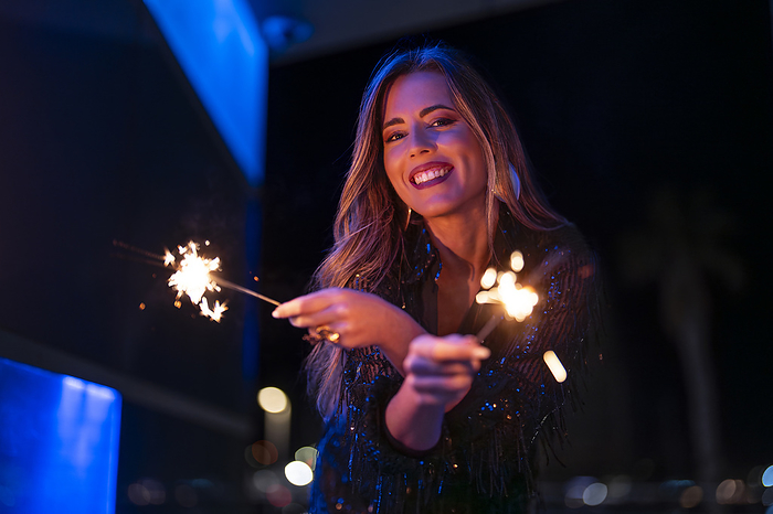 Happy woman holding sparklers at night