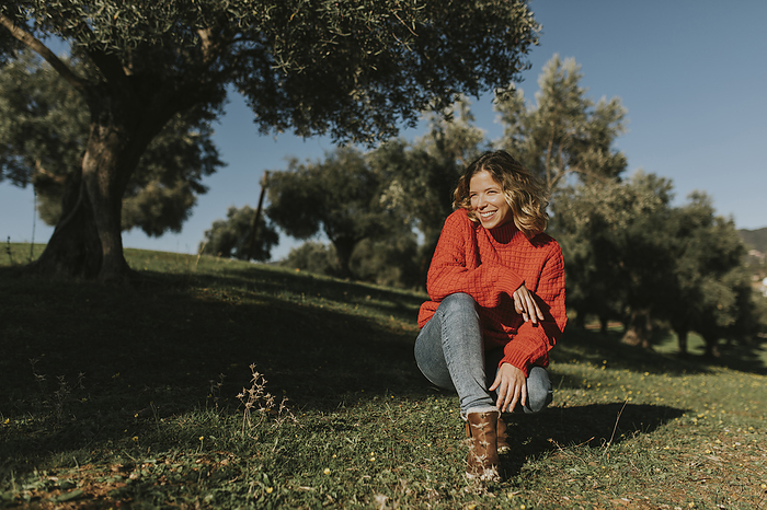 Happy woman crouching in olives field on sunny day