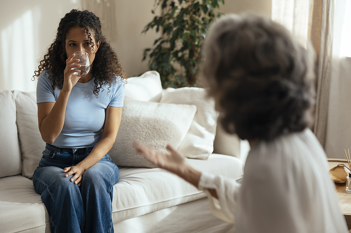 Woman drinking water and having therapy session with psychotherapist at home