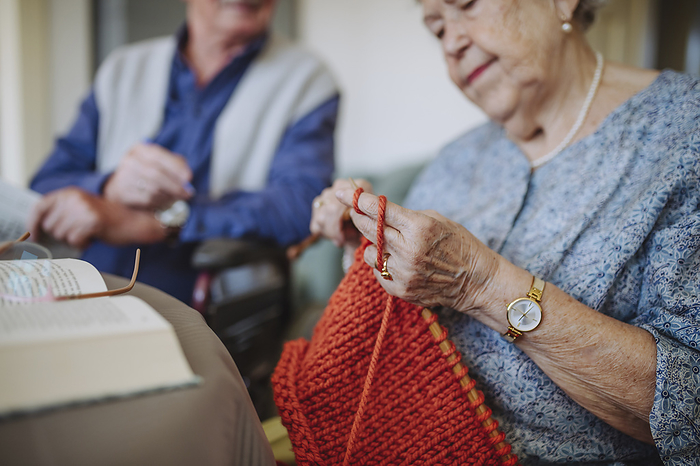Senior woman knitting wool with man sitting in background