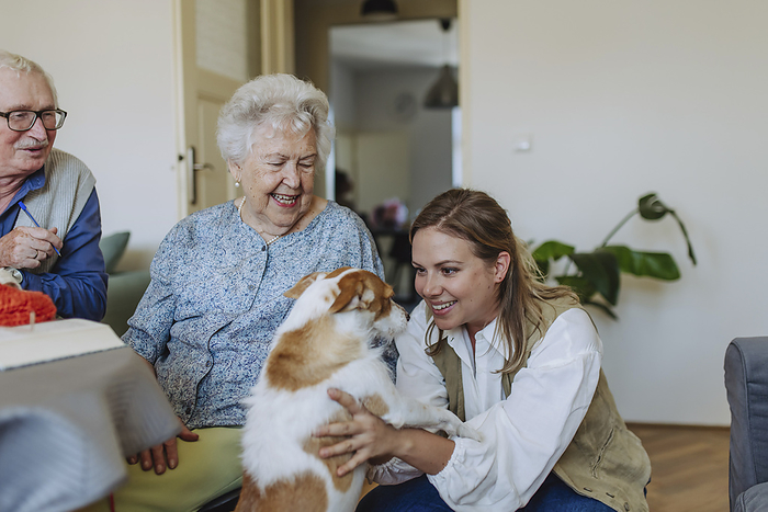 Happy senior couple with healthcare worker stroking dog at home