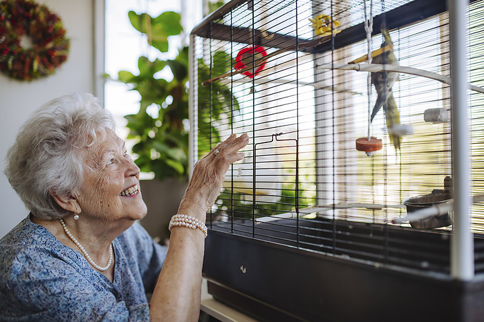 Happy senior woman looking at bird in cage at home