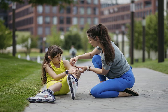 Mother helping daughter injuring herself roller skating at the city park