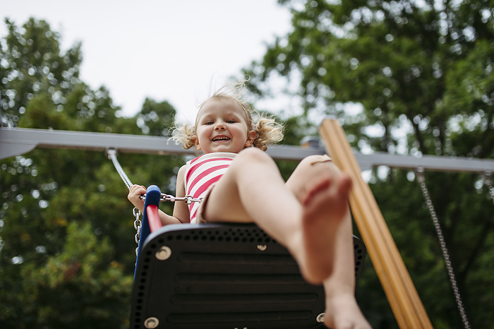 Little toddler girl and mother have fun at playground swinging on a swing