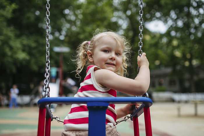 Smiling girl sitting in swing at gthe playground