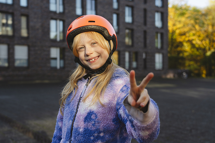 Smiling girl wearing helmet gesturing peace sign with hand
