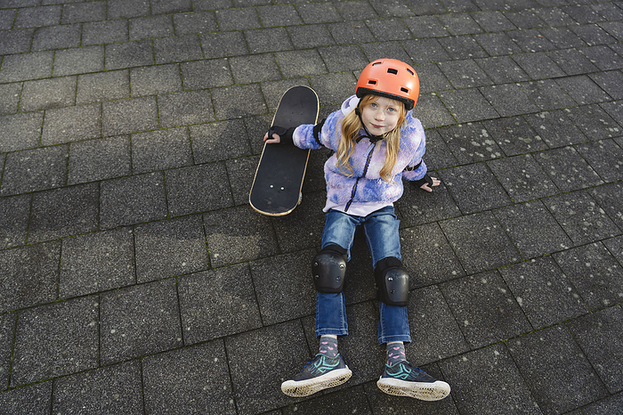 Girl sitting next to skateboard on ground