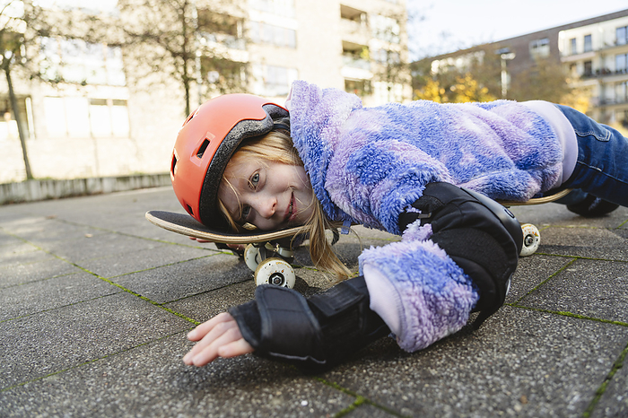 Playful girl lying over skateboard on street