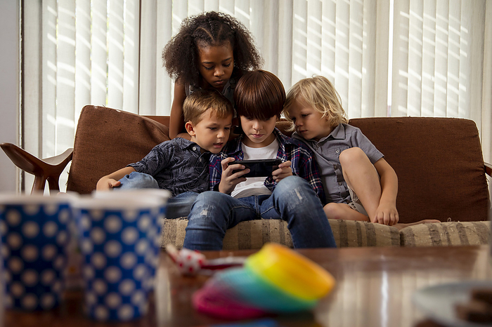 Boy playing game on smart phone with friends sitting on couch