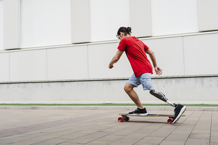 Young man with prosthetic leg riding skateboard at footpath