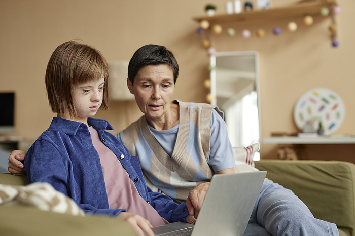 Mother teaching laptop to daughter with Down syndrome in living room