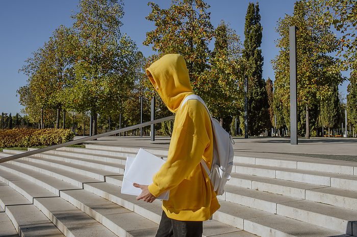 Student wearing yellow hooded shirt holding books and moving down on steps
