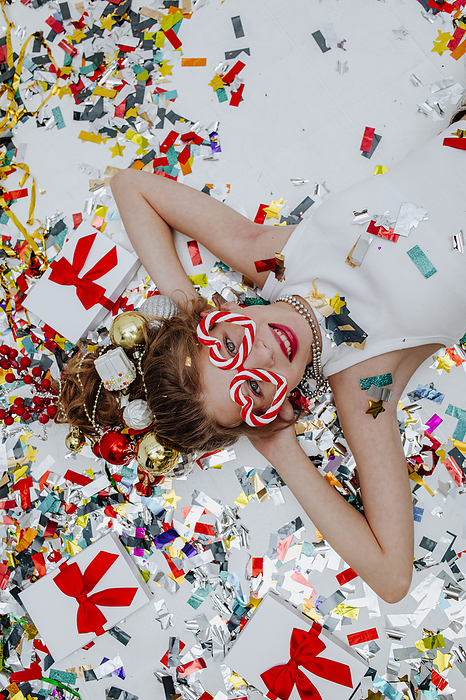 Smiling girl lying with confetti near gift boxes on white floor