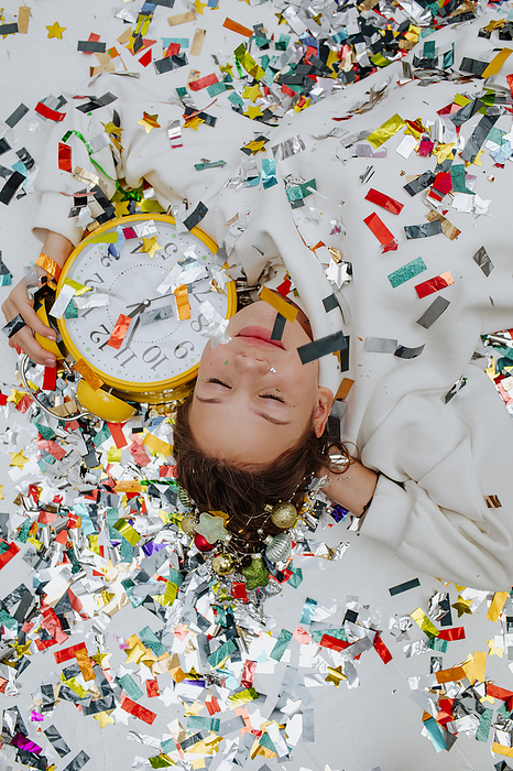 Happy girl holding clock and lying on confetti
