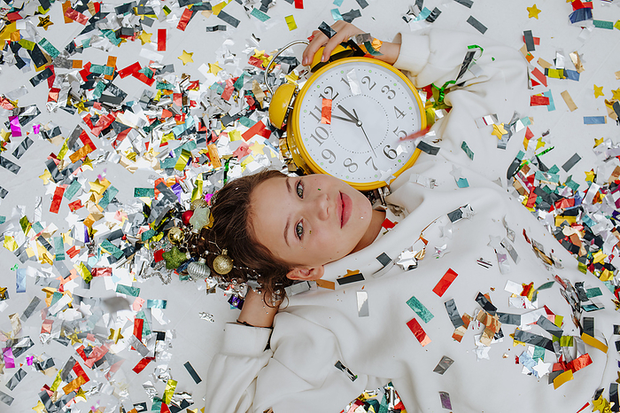 Smiling girl lying near confetti with clock on floor