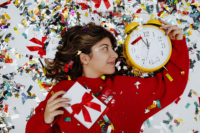 Happy girl lying near confetti with clock and gift boxes