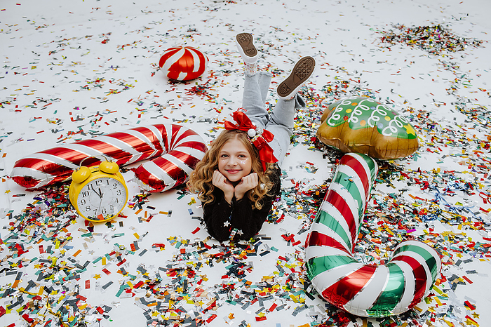 Smiling girl lying on confetti near Christmas decoration