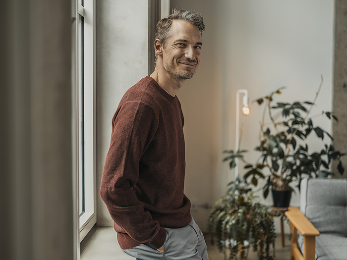 Smiling mature man leaning on windowsill at home