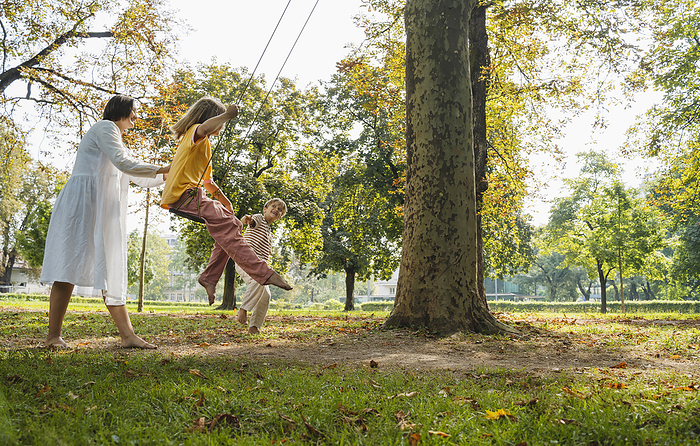 Girl swinging with mother and brother standing at park