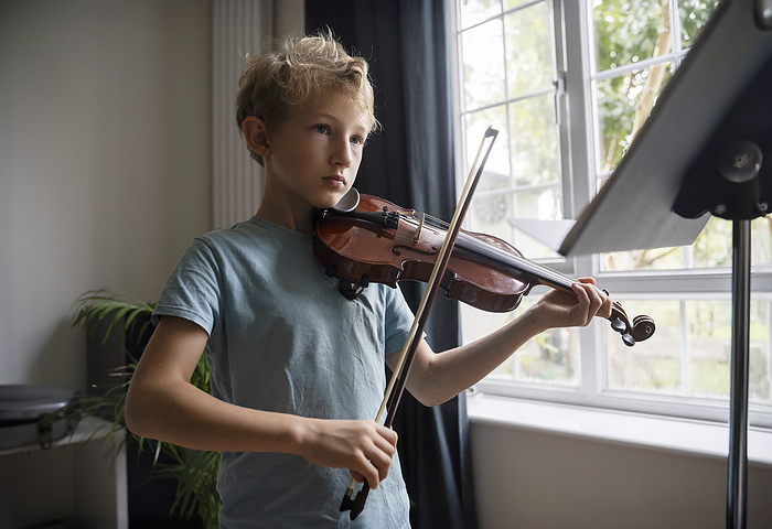 Elementary boy playing violin near window at home