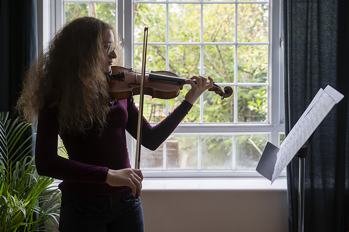 Girl playing violin in front of window at home