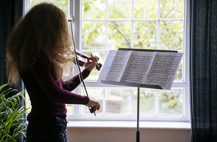 Girl practicing violin in front of window at home